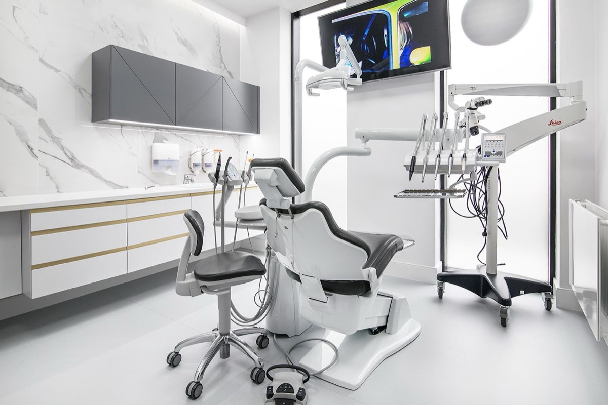 Gabinet zabiegowy Kliniki Panacea: marmurowa ściana, biały fotel stomatologiczny i mikroskop zabiegowy.